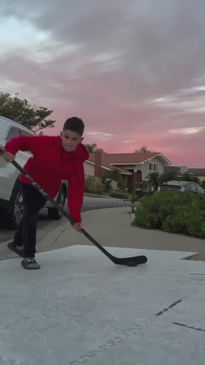 A young player shooting pucks on a driveway, the Speed Radar Gun on its tripod showing a reading